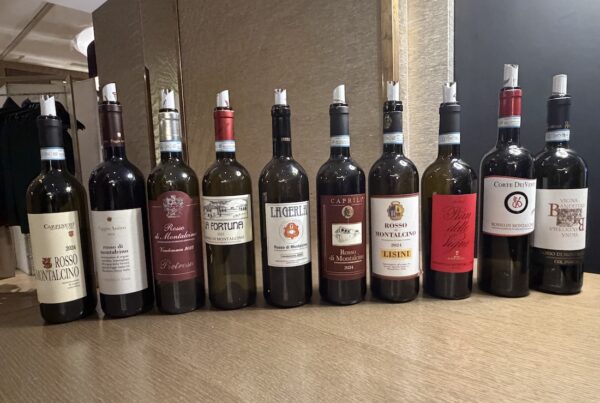 Allineamento di bottiglie di vino Rosso di Montalcino di diversi produttori sul tavolo della degustazione DoctorWine.